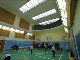 просторный освещенный спортивный зал с окнами в потолке и балконом в современной школе