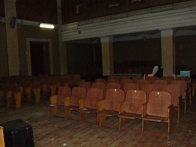 два ряда секционных деревянных кресел на полу актового зала с колонами в здании старого клуба советского времени