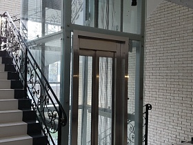 красивые фигурные черные перила на ступенях лестничных пролетов вокруг стильного стеклянного лифта в современном подъезде