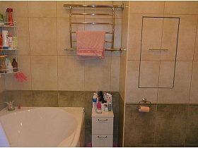 полотенцесушитель и угловая полка над белой ванной в ваной комнате с двухцветной плиткой на стене современной квартиры