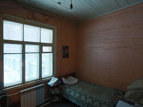 над старой кроватью с серым покрывалом и подушкой висит на стене картина