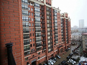 современный многоэтажный красный кирпичный дом с застекленными лоджиями, открытыми балконами в микрорайоне города