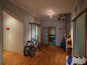 детский спортивный уголок, красный и черный велосипеды у стены светлого холла с коричневым линолеумом на полу трехкомнатной квартиры с ораньжевой кухней