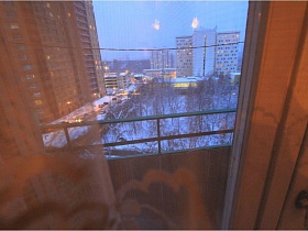 соседние высотные дома в зимнее время через стекло окна с  балконной дверью на открытый балкон с перилами квартиры бабушки и дедушки советского времени