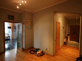 маленькие лампочки подвесной люстры на желтом потолке просторного холла с кремовыми стенами трехкомнатной семейной квартиры с ораньжевой кухней