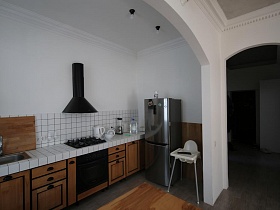 общий вид скромной и практичной кухни, входной двери и белого шкафа в прихожей из гостиной зонированной комнаты современной скандинавской квавртиры