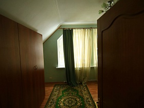 открытая дверь в спальную комнату с зеленым ковром на полу и зелеными шторами на окнах съемного двухэтажного дома в сосновом лесу