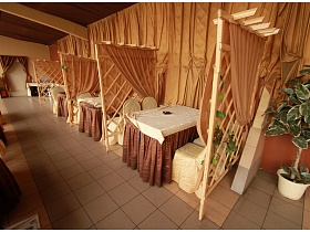 отдельные уютные зоны отдыха за решетчатой деревянной перегородкой с бежевыми шторами на открытой площадке летнего кафе на озере