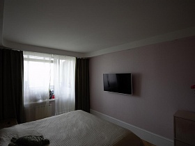 плоский телевизор на розовой стене напротив большой кровати в спальной комнате стильной трехкомнатной квартиры
