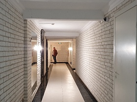 светильники у прямоугольных зеркал на стенах из белого кирпича длинного коридора в современном жилом доме
