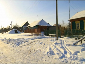 ряд жилых деревянных домов вдоль накатанной дороги в деревне зимой
