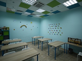 аппликация из ярких рыбок и разноцветной радуги на голубых стенах классной комнаты с партами и стульями на квадратном полу детского центра