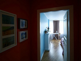 коллаж из картин на терракотовой стене прихожей у входной двери в спальную комнату уютной женской квартиры в новострое