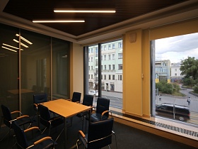рулонные жалюзи на больших окнах комнаты для переговоров с черными креслами вокруг прямоугольного стола на металлических ножках
