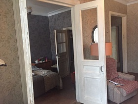 напольный торшер с оранжевым абажуром, мягкое полосатое кресло с клетчатым покрывалом, круглое зеркало на стене за открытой дверью в спальную комнату кв.24