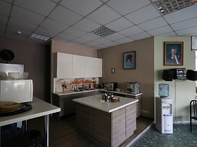 кухонный уголок на подиуме с мебельной стенкой, электроприборами и посудой на прямоугольных столах в офисном кафе
