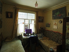две кровати у стен, стул, стол с ноутбуком у окна с открытой фороточкой спальной комнаты деревянной советской дачи художника с овальной террасой