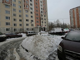ствол дерева под снегом на повороте дороги внутри двора высотных зданий