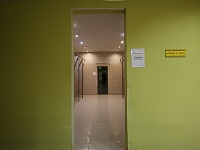 бежевая плитка на полу и стенах освещенной душевой и сауны через открытые двери в стенах салатового цвета раздевалки
