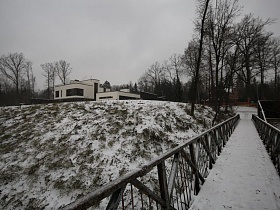 белые стены зданий на пригорке у длинного подвесного пешеходного моста с перилами в зимнее время