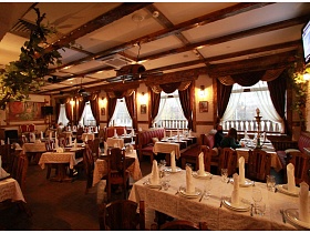 общиц вид уютного зала ресторана, увитого виноградной лозой, с сервированными столиками по центру и у больших окон ресторана с кавказким интерьером