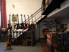гитары, закреплены на стойках у металлической лестницы с деревянными ступенями и перилами на второй этаж музыкального магазина на территорииотдельного здания с собственным двором