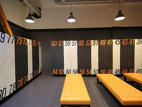 длинные ораньжевые банкетки напротив шкафчиков с черными и ораньжевыми номерами в ораньжевой спортивной раздевалке