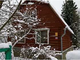 красивая двухэтажная бревенчатая дача в коричневом цвете с высоким цоколем на зимнем участке