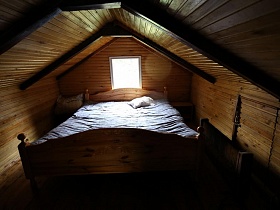большая деревянная кровать с белым одеялом и подушкой, прикраватными тумбочками на мансарде небольшого домика среди новостроек