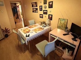 светлые металлические стулья у обеденного стола с белой скатертью, телевизор и картина на столе у стены с фотографиями в рамках бежевой кухни современной квартиры молодоженов на втором этаже