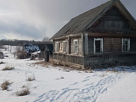 покосившейся старый деревянный дом с треугольной крышей в заброшенной деревне со снегом на просторном участке