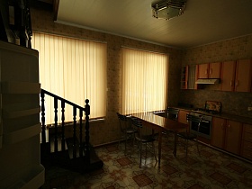 металлические стулья со спинкой у коричневого обеденного стола, мебельная стенка в бежевой кухне двухэтажного дома под съем в сосновом лесу