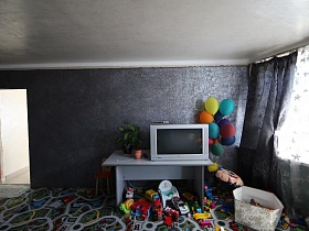 белый телевизор, комнатный цветок на белом письменном столе, детские игрушки под столом и в корзине, связка разноцветных шаров в детской комнате,с незаконченным ремонтом семейной дачи с видом на город
