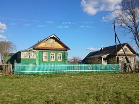 зеленый деревянный дом под треугольной крышей с огромной верандой, резными наличниками на окнах за штакетным зеленым забором в старой деревне 2