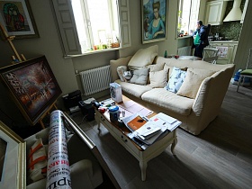 разнопланновые картины в рамках на кресле, на мольберте, стене, на полу, напротив журнального столика в зоне отдыха гостиной современной дизайнерской квартиры
