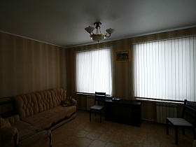 бежевые полосатые обои на стенах гостиной с бежевой мягкой мебелью и бежевым линолеумом на полу двухэтажного пустого дома под съем в сосновом лесу
