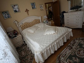 овальные ковровые цветные дорожки у кровати с белым стеганным покрывалом и подушками в спальне большой квартиры врача