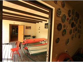 открытая дверь с предбанника на террасу со столом, скамейками и раскладушкой на коричневом полу деревянной постройки с сауной на даче работника кино