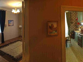 вид на светлую гостиную с торшером у стены с картинами, синими шторами на окнах, бежевым с коричневым ковром и на зеленую кухню с мебельной стенкой и обеденным столом из прихожей кв 27