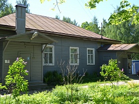 деревянное одноэтажное здание под красной крышей с двумя отдельными входами на территории зеленого участка с двухэтажной деревянной школой 19 века