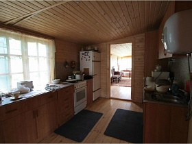белый холодильник, газовая плита, нагревательный бак и коричневая кухня в просторной деревянной кухне дачи