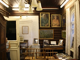 большие портреты и картины на стенах, маленькие на столе, этажерке, тумбочке, деревянные стулья со спинками, деревянный шкаф у стены деревянной комнаты советской художественной дачи-музей