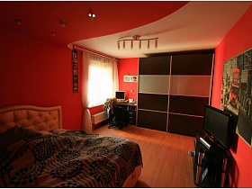 картина на стене над телевизором,коричневый шкаф-купе в спальной комнате с розовыми стенами в современой трехкомнатной квартиры необычной планировки