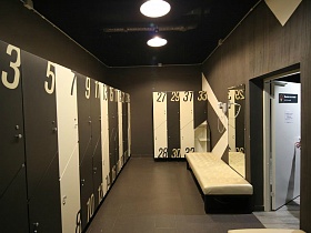 черно белые дверцы шкафчиков пронумерованные в черной спортивной раздевалке с большим зеркалом на стене