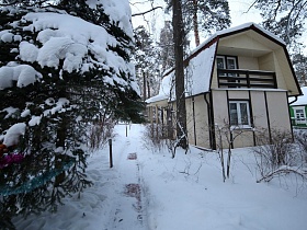 снег на крыше красивого двухэтажного современного домика на дачном участке в лесу зимой