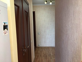 открытая дверь из кухни в прихожую с бежевыми обоями на стенах и коричневым линолеумом под дерево на полу двухкомнатной квартиры