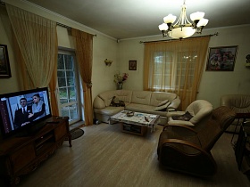 картины на светлых стенах, телевизор на деревянной тумбочке у входной двери в гостиную семейного дома в глухом лесу