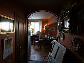 сушилка для белья, картины у коричневой стены коридора с арочным дверным проемом на кухню с круглым обеденным столом и стульями со спинкой на полу с квадратной коричневой плиткой