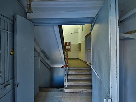 освещенная лестничная площадка первого этажа с бетонными ступенями лестницы с перилами в сером подъезде дома советского времени