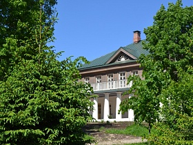 Старинная двухэтажная деревянная школа 19 века с открытой террасой над крыльцом с белыми колоннами в окружении зелени